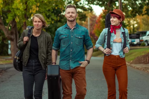 three people walking down a street carrying instrument cases
